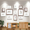 A set of thirteen wooden picture frames with various sizes and orientations displayed on a light gray wall.