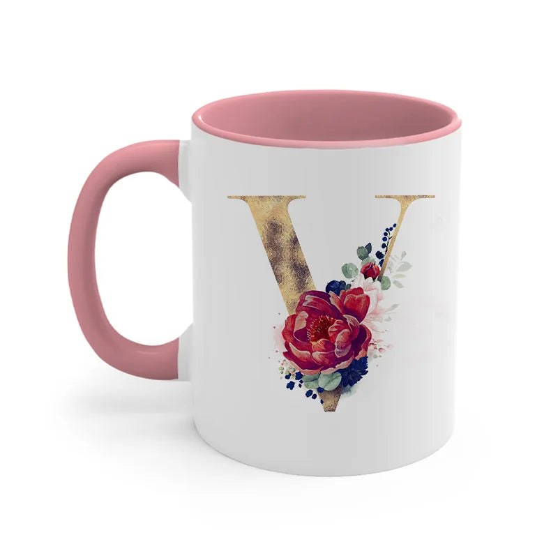 A pink ceramic coffee mug featuring a gold letter V design with watercolor floral accents.