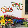 Handcrafted metal gecko wall art featuring colorful, vibrant geckos displayed above a garden bed.