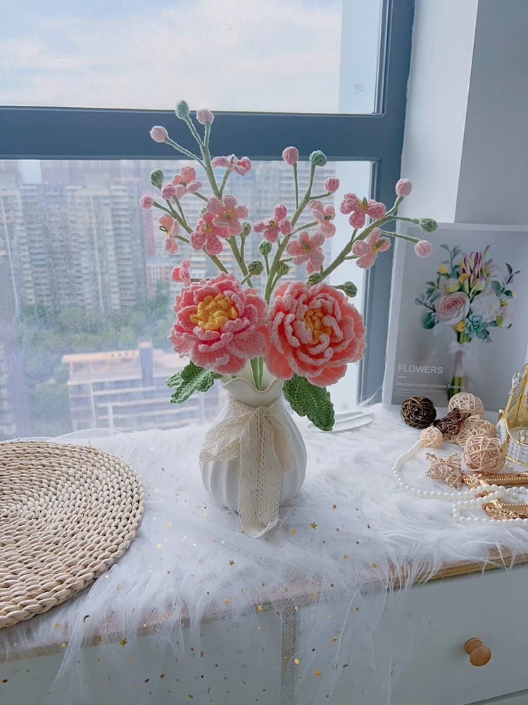 A bouquet of handmade crochet flowers in shades of pink and yellow displayed on a white table.