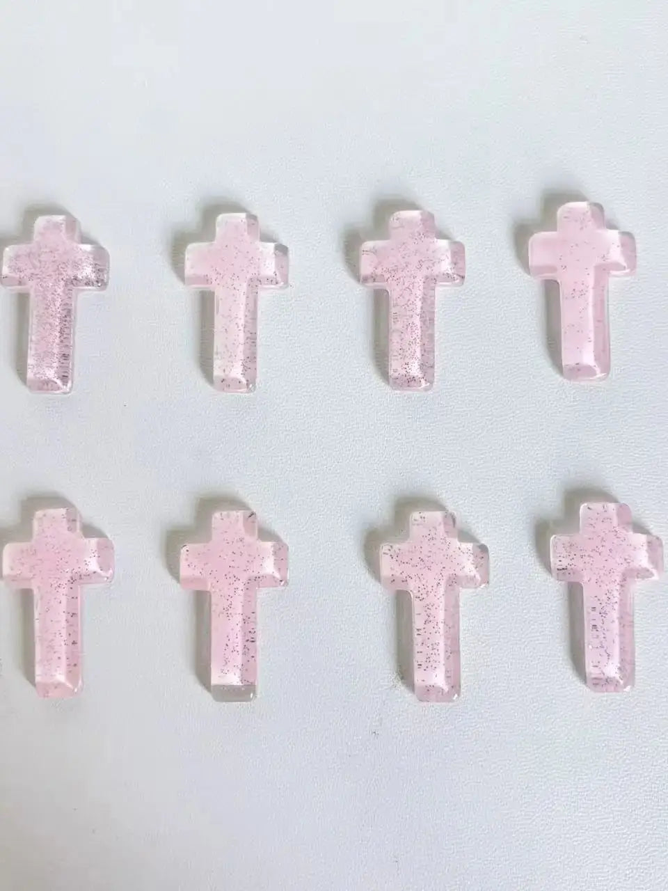 Eine Ansammlung von rosa Glitzerkristallkreuzdekorationen in einem Raster.