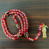 A red and gold Santa Muerte rosary necklace with beads and a pendant is displayed on a dark wooden surface.