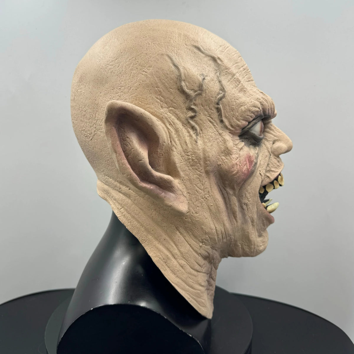 A realistic demon latex mask with sharp teeth displayed on a black mannequin head.