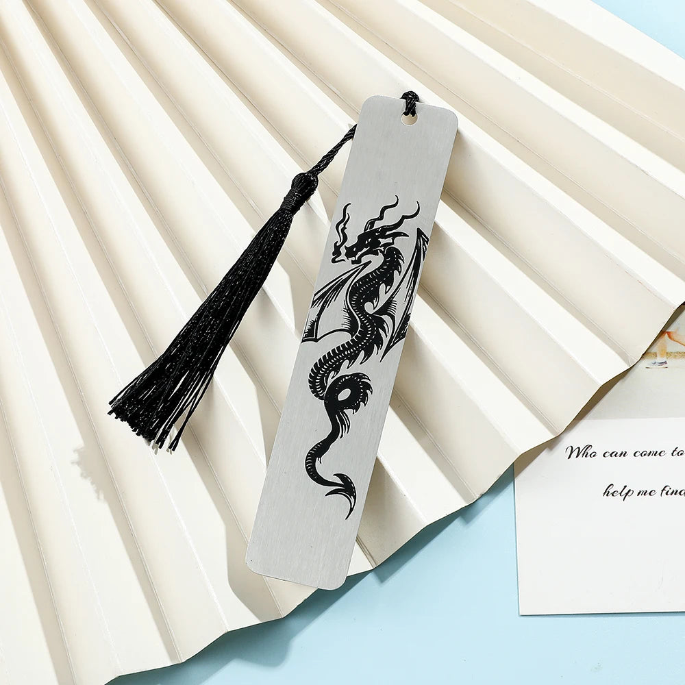 A silver bookmark featuring an engraved black dragon design with a tassel, placed on a light background.