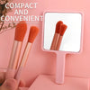 Two pink makeup brushes displayed in front of a handheld vanity mirror.