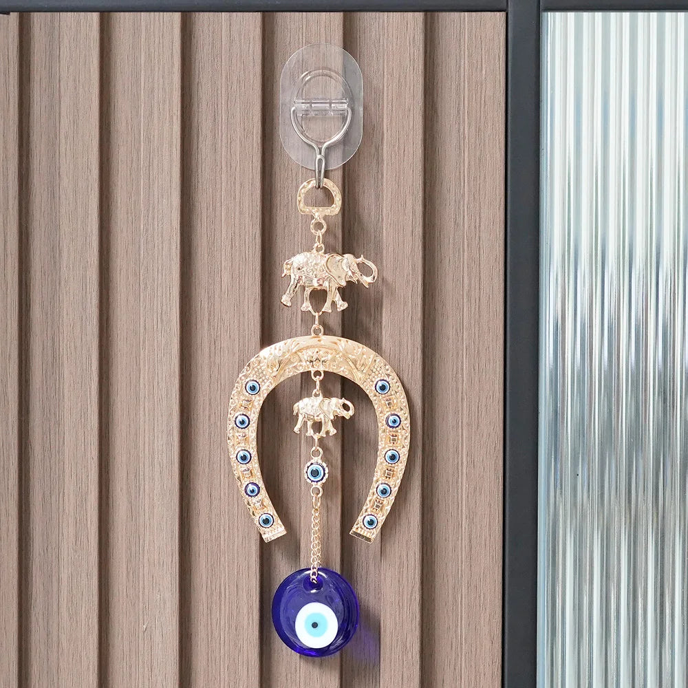 A gold and blue amulet featuring an elephant charm and a blue eye, hanging on a wall.