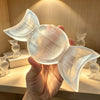 A hand holds a translucent white selenite triple moon charging bowl illuminated by soft light.