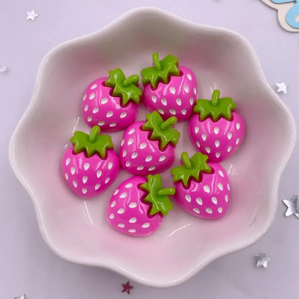 Pink strawberry resin flatback charms with green tops arranged in a white dish.