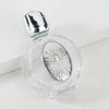 Decorative glass bottle with a silver figurine and a twist cap resting on a white surface.