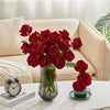 A bouquet of deep red velvet artificial roses in a glass vase on a white table.