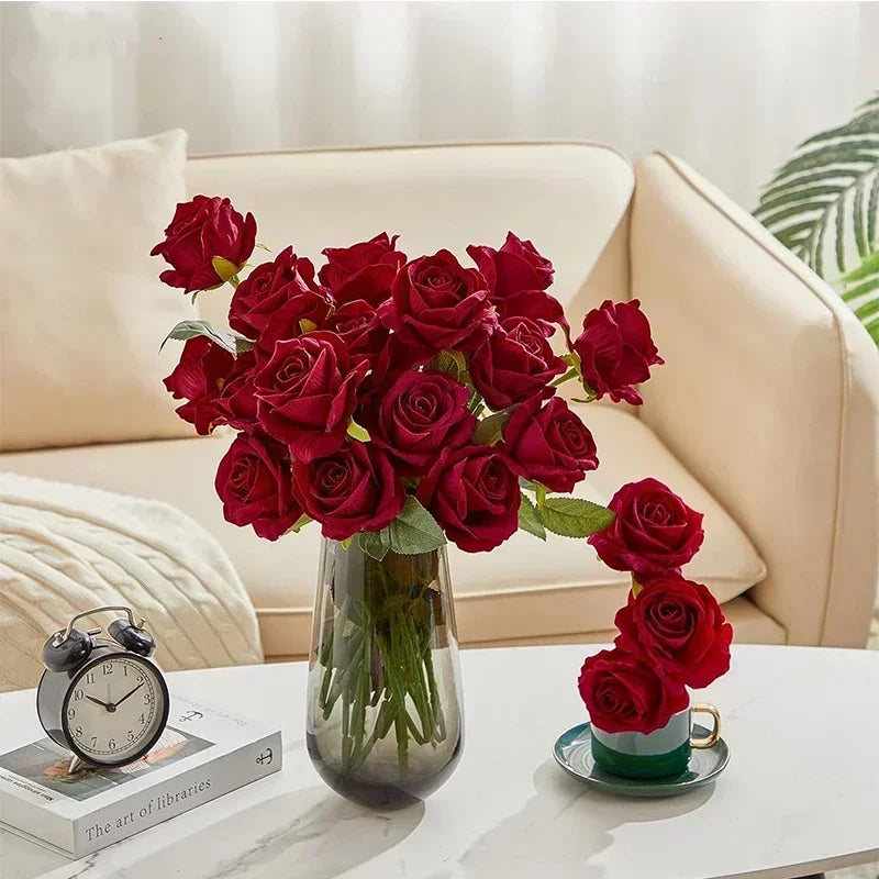 A bouquet of deep red velvet artificial roses in a glass vase on a white table.
