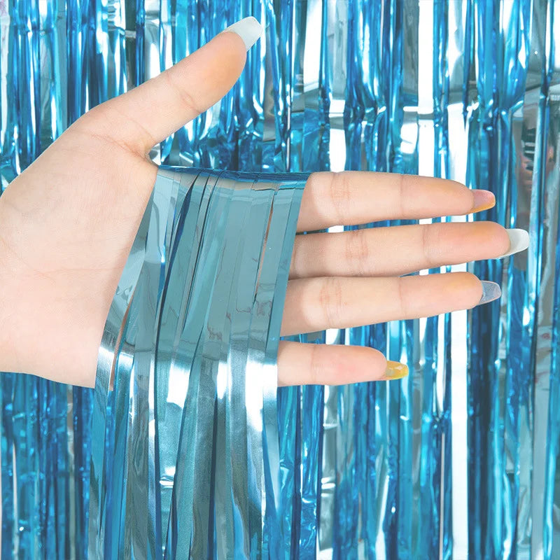Hand holding a strip of silver metallic foil fringe curtain backdrop against a blue background