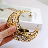 A hand holds a gold metallic crescent moon candle holder with a star charm.