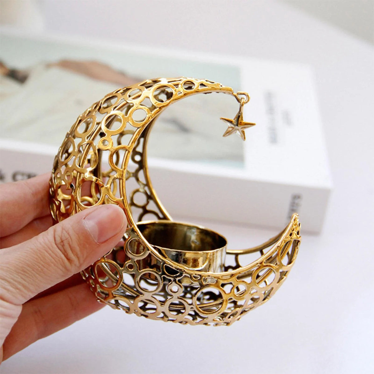 A hand holds a gold metallic crescent moon candle holder with a star charm.