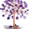 A crystal money tree decor featuring purple amethyst crystals on a wooden branch and a light stone base.