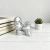Silver resin sculpture of a kissing couple resting on a white wooden surface next to a potted succulent plant.