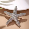 A sparkling silver starfish brooch pin set resting on a beige surface with soft shadows.
