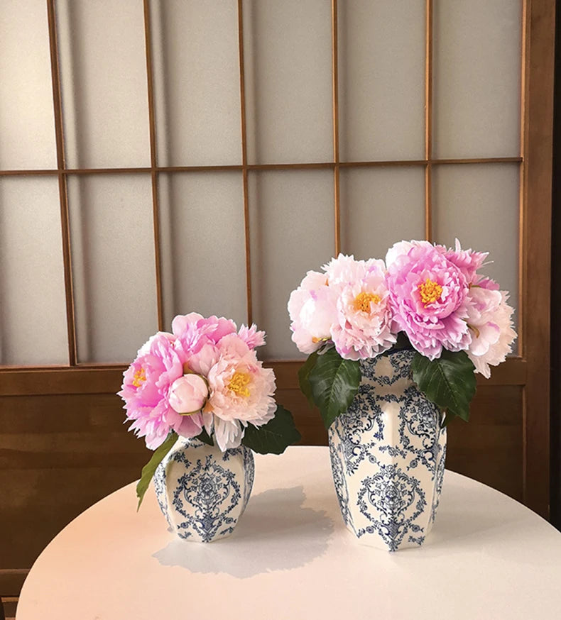 A floral arrangement of pink peonies in a blue and white porcelain vase set on a white table.