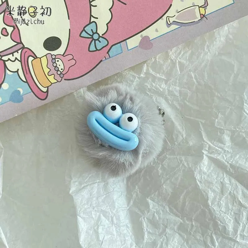 A small, light blue plush sausage-mouth keychain with large white eyes resting on crumpled white paper.