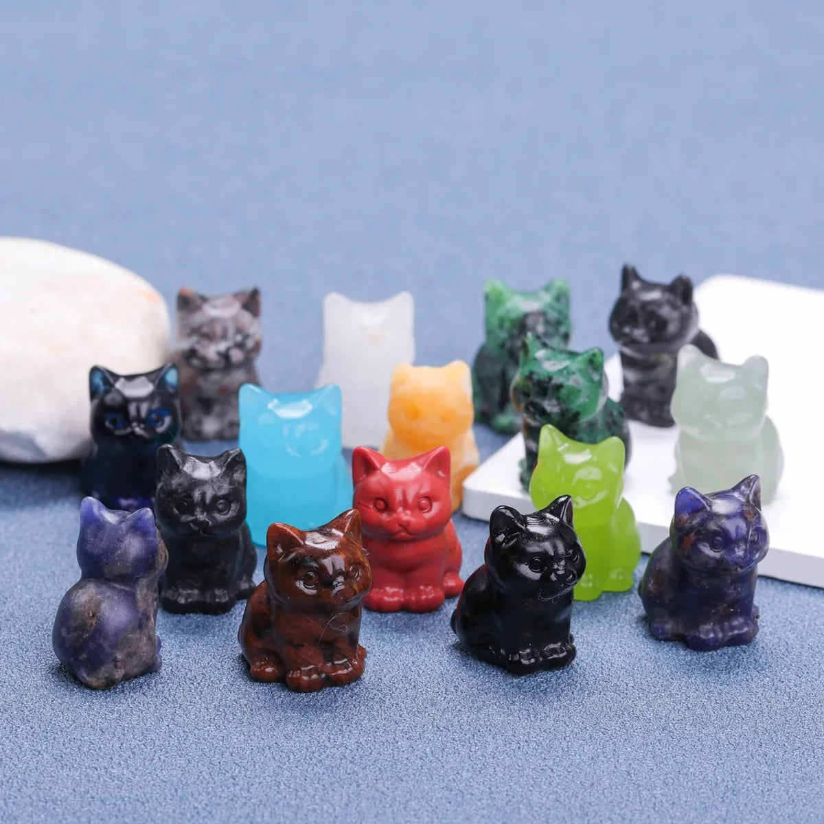 Collection d'ornements de chats en cristal sculptés à la main, de différentes couleurs et nuances, disposés sur une surface b