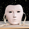 A pale pink ancient style masquerade mask with delicate lines resting on a wooden surface.