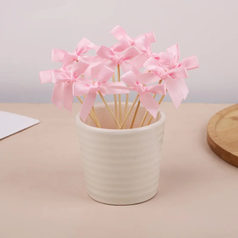Pink bow cupcake toppers in a white cup displayed on a light surface.