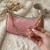 A pink velvet pouch with a gold chain and a pink glass stone charm is held in a hand on a fluffy white surface.
