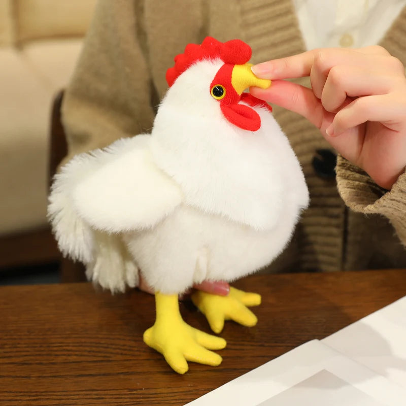 A white plush rooster toy with a red comb and yellow feet is being touched by a person's finger.