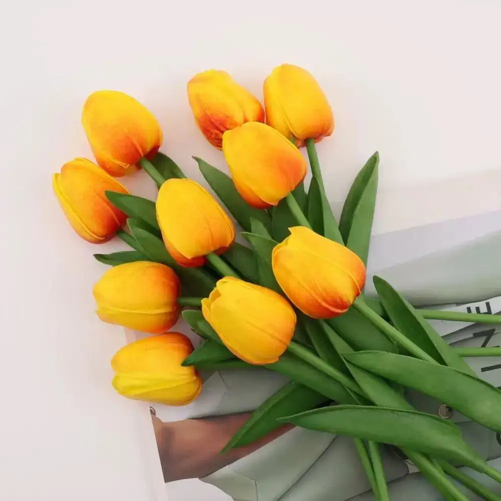 A bouquet of realistic artificial yellow and orange tulips with green leaves.