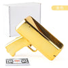 A gold-colored funny money shooter toy gun next to its white box and a stack of dollar bills.