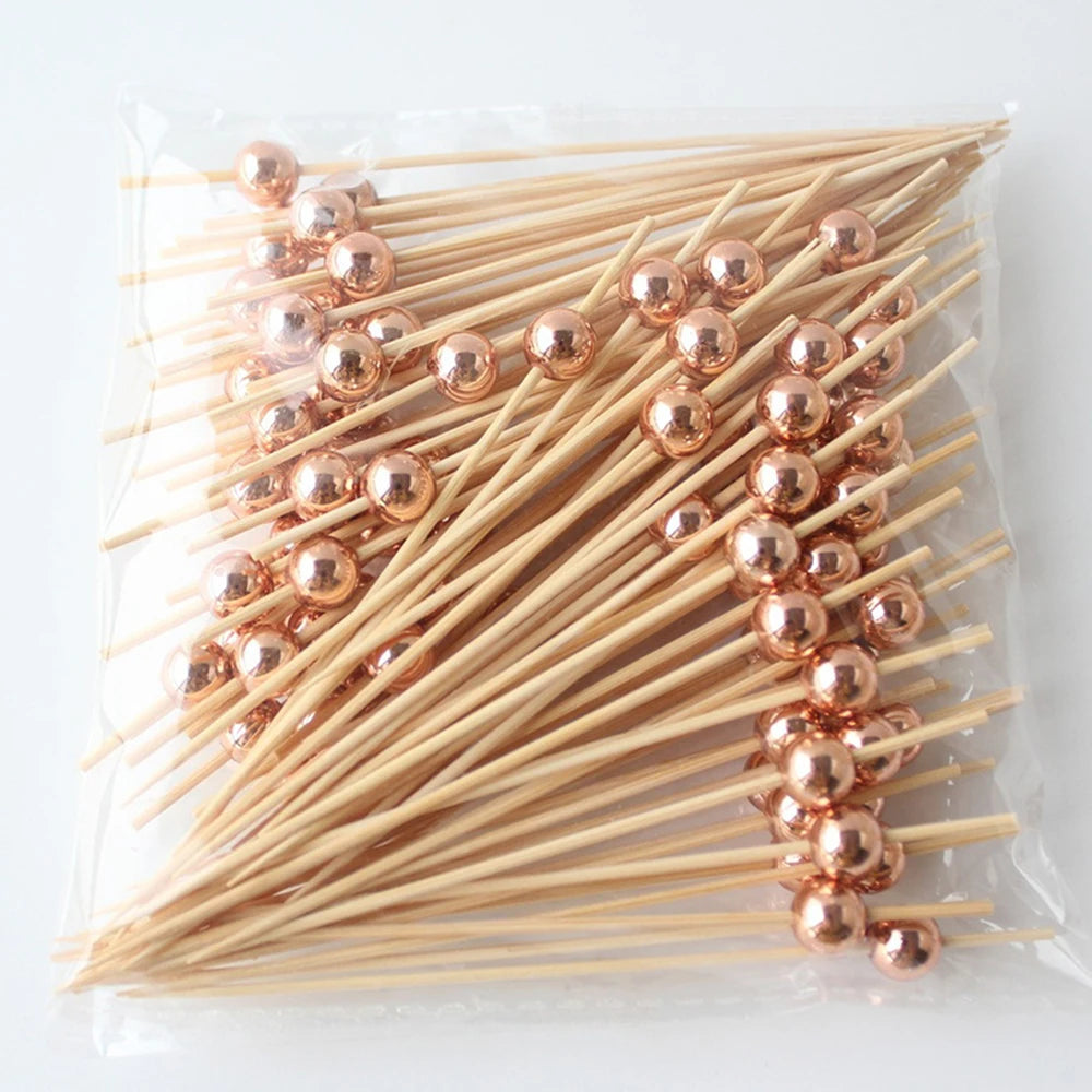 A bundle of bamboo fruit skewers with gold-colored spherical beads, laid out in a clear plastic bag.