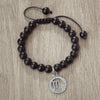 A black beaded bracelet with a silver zodiac sign charm is displayed on a wooden surface.