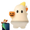 A white ghost phone decoration charm with a pumpkin face and an orange ear, next to a smartphone.