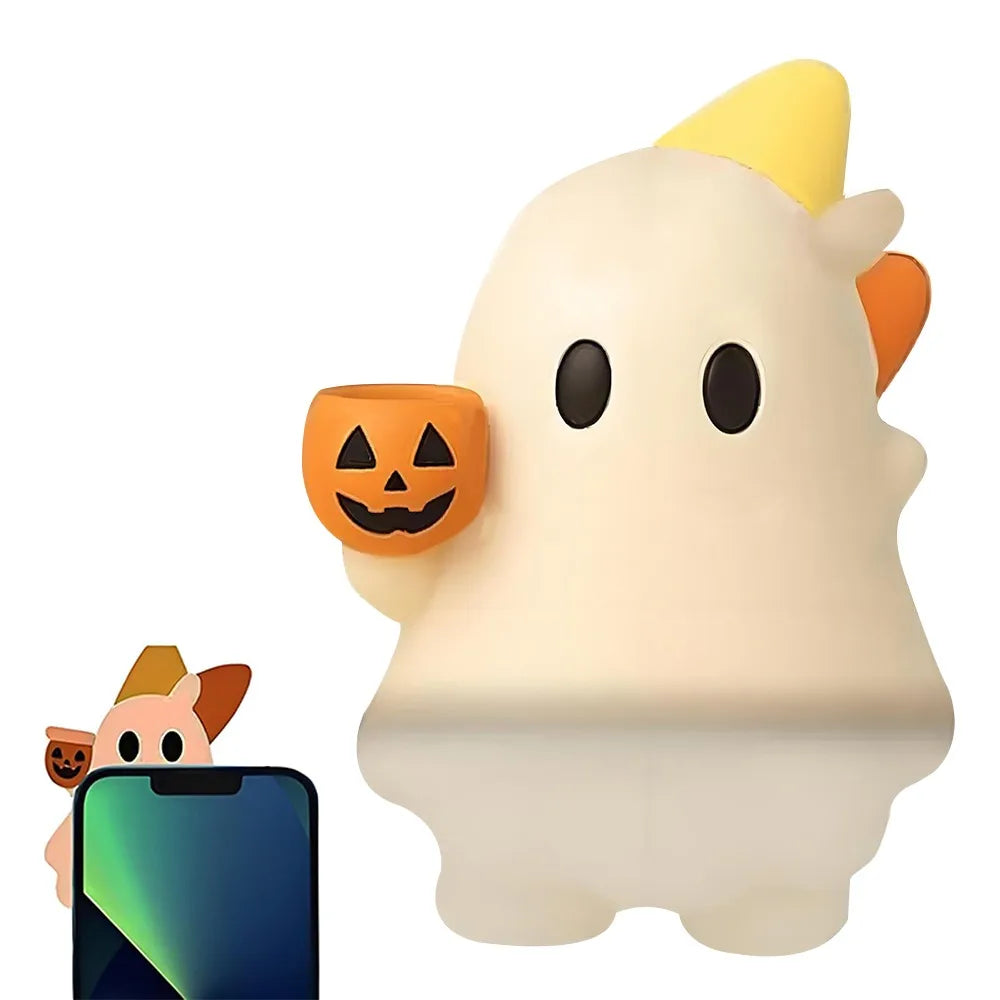 A white ghost phone decoration charm with a pumpkin face and an orange ear, next to a smartphone.