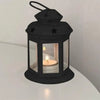 A black vintage hanging metal lantern with a glass enclosure and a lit candle.