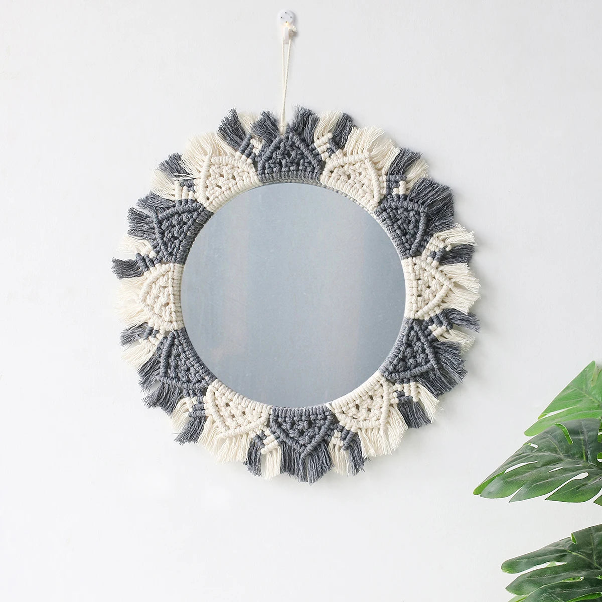 A round macrame wall mirror with a bohemian fringe border in gray and cream.