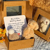 Un oso de peluche mini y una tarjeta de inspiración presentados en una caja de cartón para regalo.