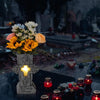 A dark stone vase with an illuminated cross holds a floral arrangement on a grave plot.