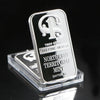 A silver Troy ounce fine silver mint bar with a stylized 'T' design, displayed in a clear plastic holder.
