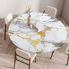 A round marble print tablecloth with gold veining is set on a wooden table surrounded by modern chairs.