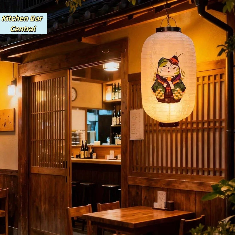 A large, round, white paper hanging lantern with a cat face is displayed in a wooden restaurant setting.