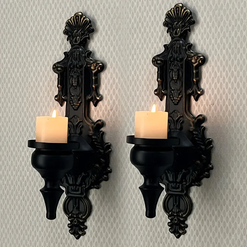 A set of two vintage wrought iron wall-mounted candle holders with black bases and lit candles.