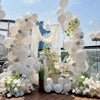 A floral and balloon decoration setup featuring white, gray, and light green balloons and flowers for a party.