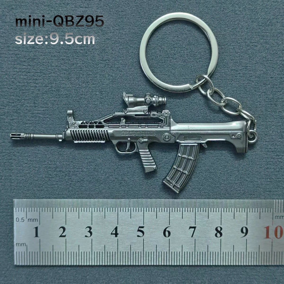 A silver alloy gun model miniature keychain with a realistic finish, shown next to a ruler.