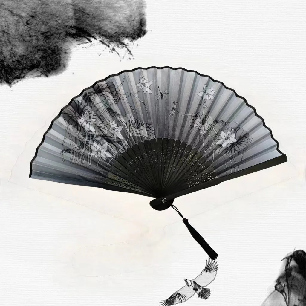 A black vintage bamboo folding hand fan with delicate floral designs is open against a bright sky.