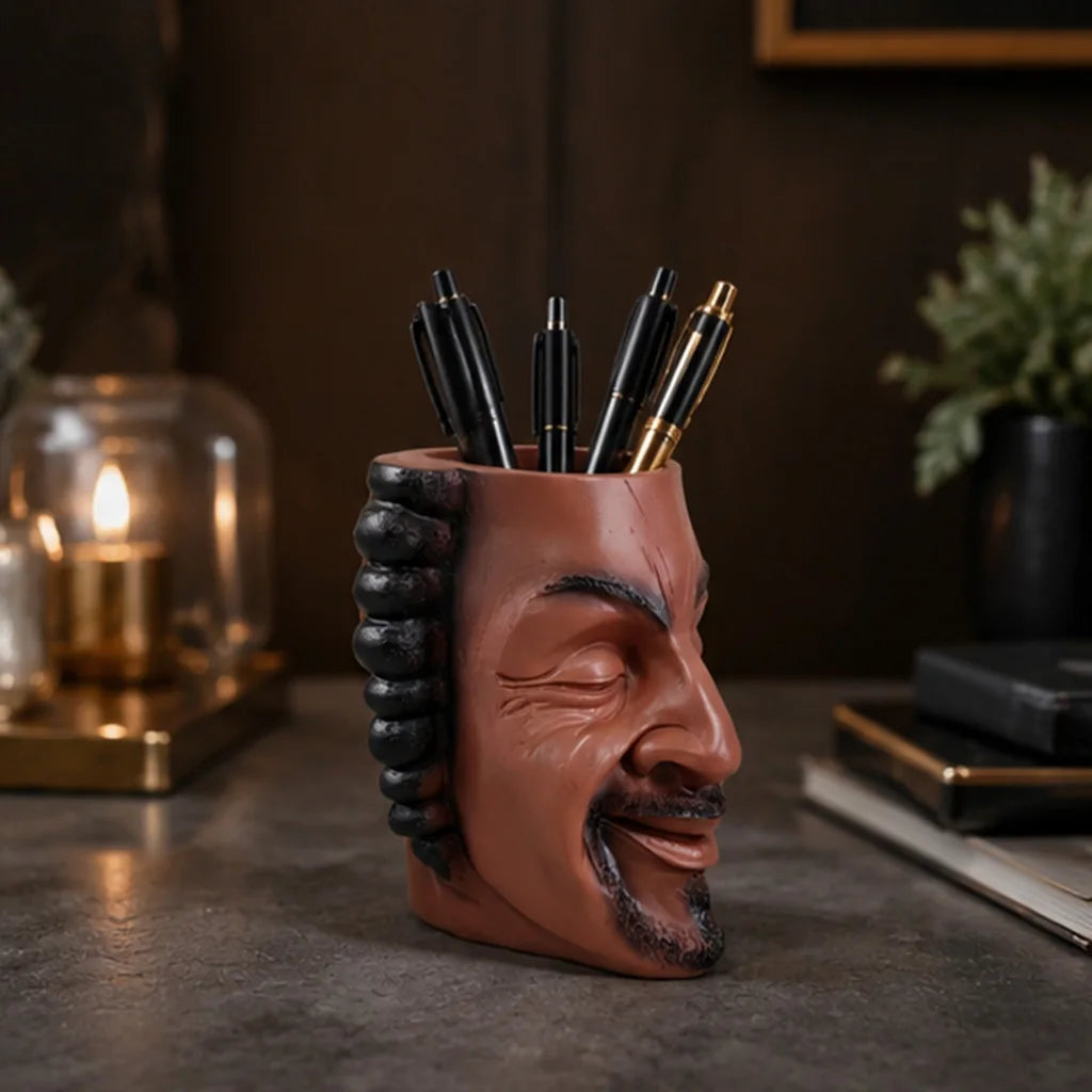 A terracotta-colored artistic face planter pot holds several black and gold pens on a dark surface.