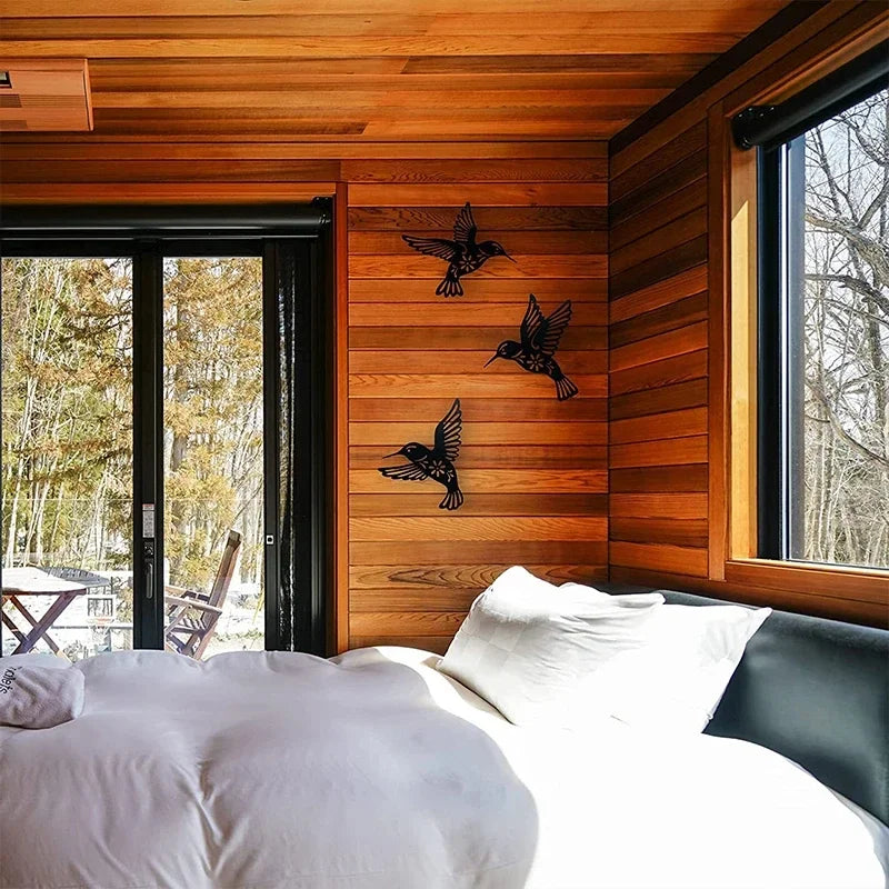 A bedroom featuring a wooden wall panel with metal hummingbird wall decor above a window.