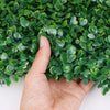A hand is holding a dense green artificial grass hedge panel for privacy and decor.
