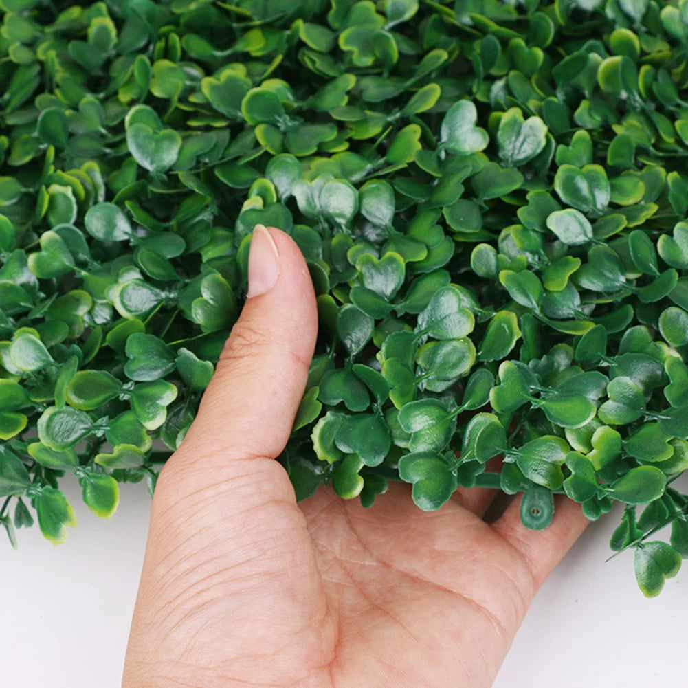 A hand is holding a dense green artificial grass hedge panel for privacy and decor.