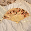 A folding hand fan with a leopard print design and black handle rests on white fabric.